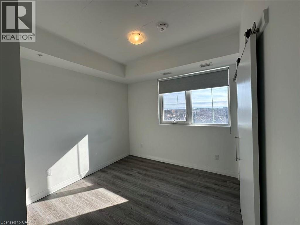 This property features a room with wood-style flooring, a window with a roll-down blind, and a sliding barn door - 108 Garment Street S Unit# 708, Kitchener, ON - Indoor Photo Showing Other Room