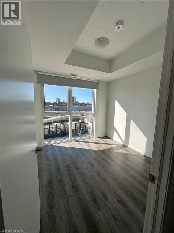 This room features a window with a roller shade, wood-look flooring, and a ceiling light fixture - 108 Garment Street S Unit# 708, Kitchener, ON - Indoor Photo Showing Other Room