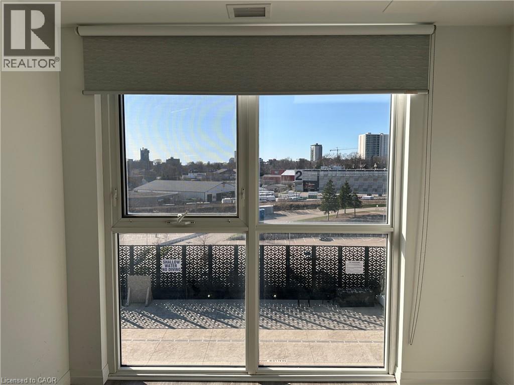 The property features a window with a roller shade, offering views of the surrounding urban landscape and a patterned privacy screen on the patio - 108 Garment Street S Unit# 708, Kitchener, ON - Indoor Photo Showing Other Room