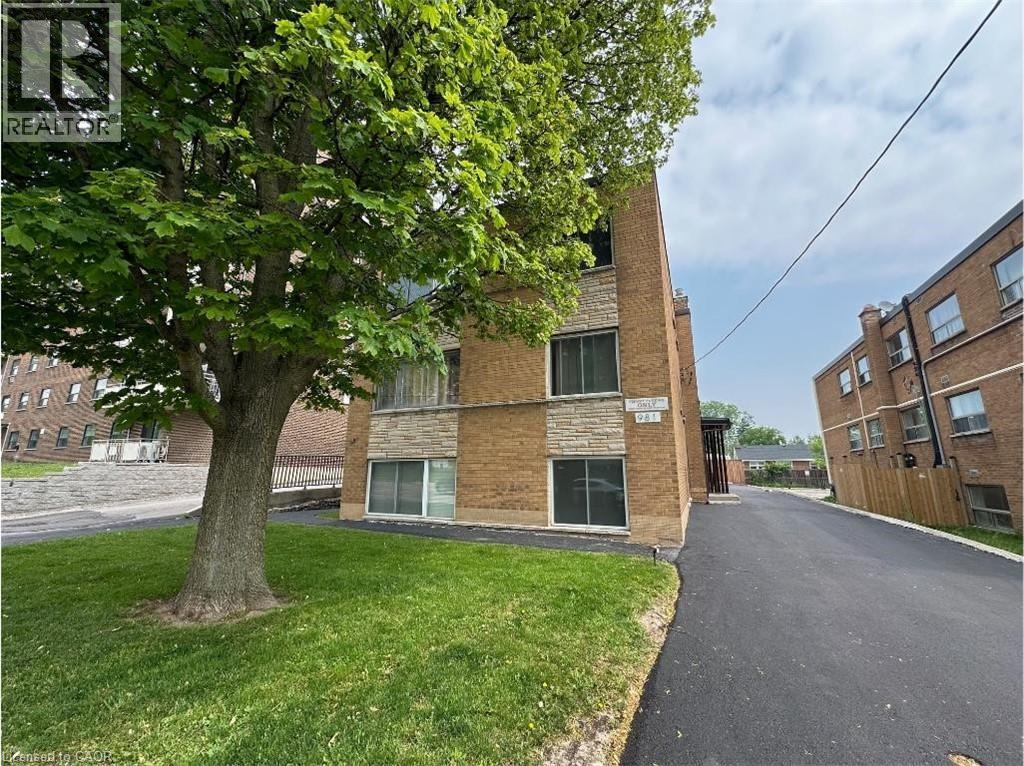 The property features a brick exterior with stone accents, a well-maintained lawn with a mature tree, and a paved driveway - 981 Mohawk Road E, Hamilton, ON - Outdoor