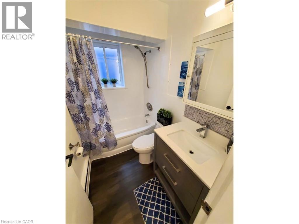 Well-appointed bathroom featuring a vanity with a white countertop and a modern faucet, dark wood-style flooring, and a tiled shower surround - 981 Mohawk Road E, Hamilton, ON - Indoor Photo Showing Bathroom