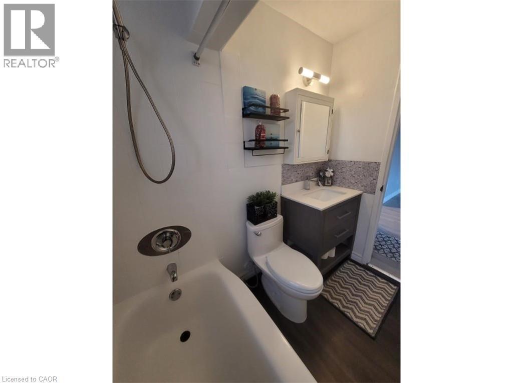 Bathroom featuring a white bathtub, a toilet, and a vanity with a white sink and gray cabinetry - 981 Mohawk Road E, Hamilton, ON - Indoor Photo Showing Bathroom