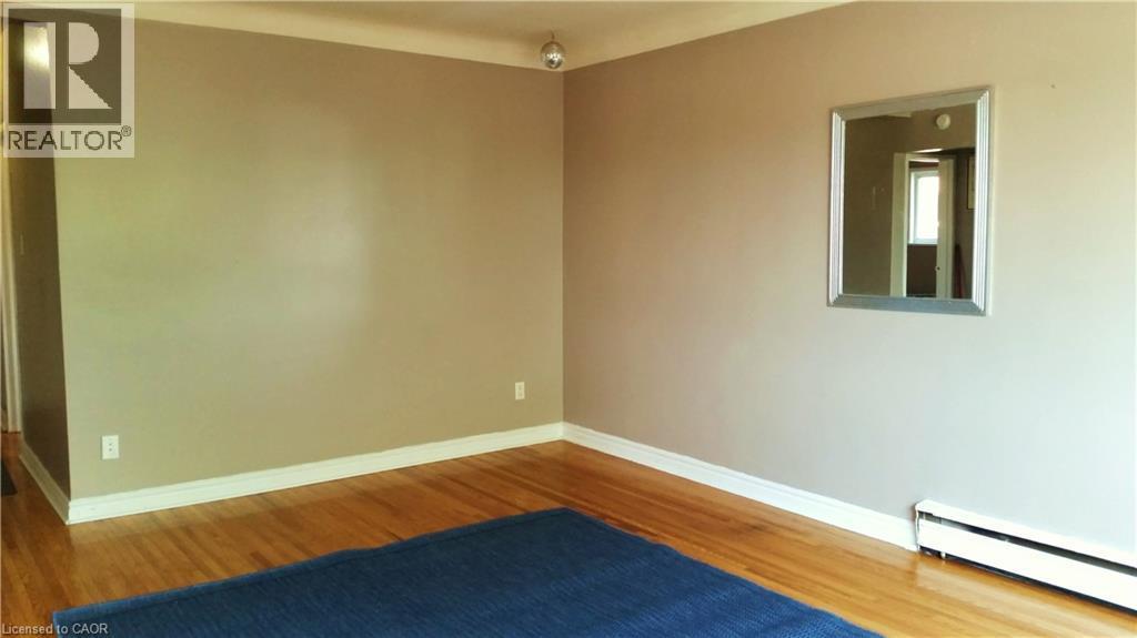 This living space features hardwood flooring, neutral-toned walls with white trim, and a wall-mounted mirror - 981 Mohawk Road E, Hamilton, ON - Indoor Photo Showing Other Room