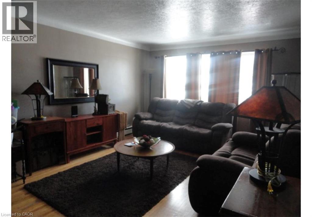 This living space features hardwood flooring, a large area rug, and windows with drapes - 981 Mohawk Road E, Hamilton, ON - Indoor Photo Showing Living Room