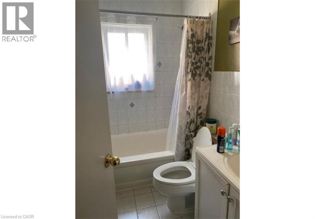 Bathroom featuring a bathtub with a shower, a toilet, a vanity with a sink, and tiled walls and floors - 981 Mohawk Road E, Hamilton, ON - Indoor Photo Showing Bathroom
