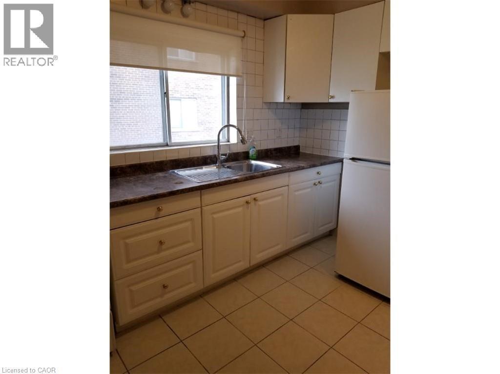 Kitchen featuring a window, white cabinetry, a stainless steel sink with a gooseneck faucet, a refrigerator, and tiled flooring - 981 Mohawk Road E, Hamilton, ON - Indoor Photo Showing Kitchen With Double Sink