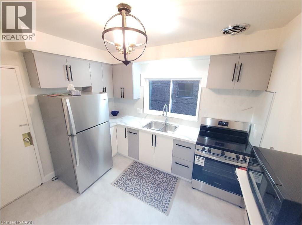 The kitchen features stainless steel appliances, including a refrigerator and range, light-colored cabinetry with dark hardware, and a double basin sink - 981 Mohawk Road E, Hamilton, ON - Indoor Photo Showing Kitchen