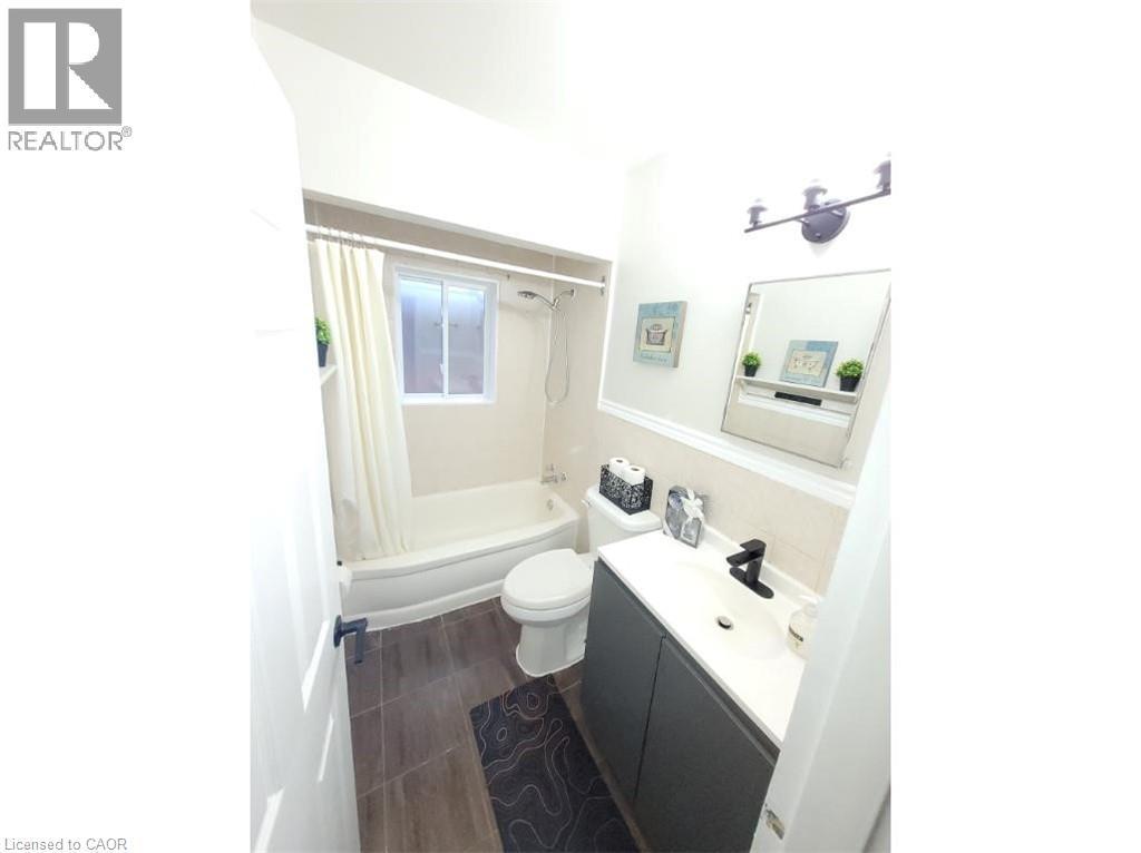Bathroom featuring a vanity with a white countertop and a black faucet, a toilet, and a bathtub with a window - 981 Mohawk Road E, Hamilton, ON - Indoor Photo Showing Bathroom