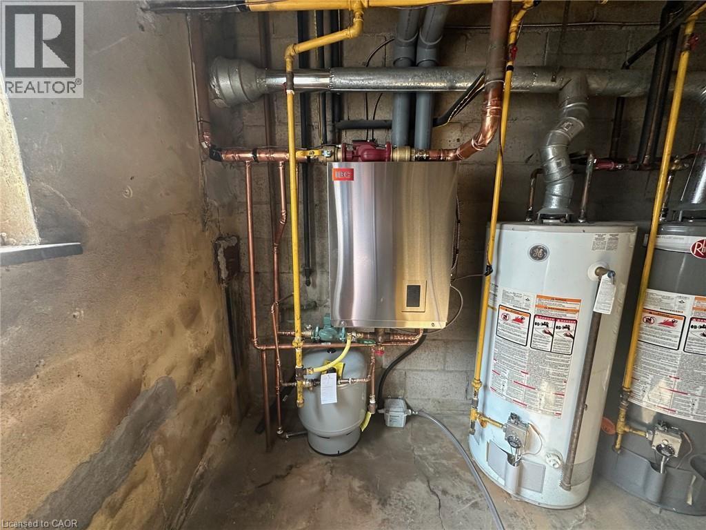 The property features a tankless water heater, water heaters, and exposed copper and yellow piping - 981 Mohawk Road E, Hamilton, ON - Indoor Photo Showing Basement
