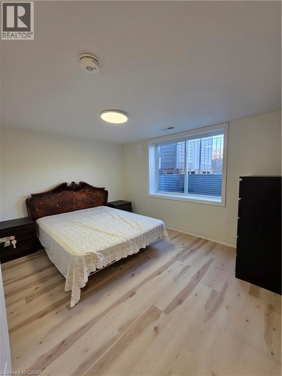 This room features light-toned wood flooring, a window with horizontal blinds, and a ceiling-mounted light fixture - 62 Richwill Road Unit# Lower, Hamilton, ON - Indoor Photo Showing Bedroom