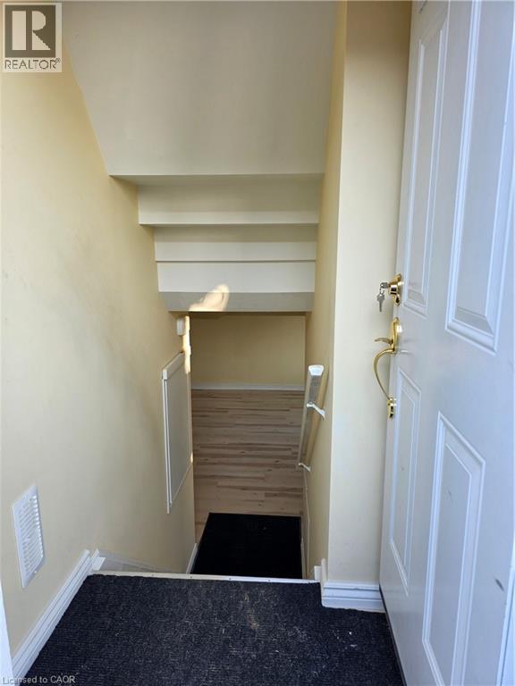 Entryway with white door featuring brass hardware, leading to a carpeted staircase with white trim, and light wood flooring visible at the bottom - 62 Richwill Road Unit# Lower, Hamilton, ON - Indoor Photo Showing Other Room