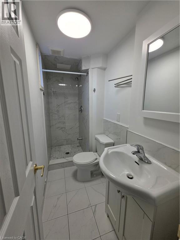 This bathroom features a shower with marble-patterned tile, a vanity with a white sink, and light-colored tile flooring - 62 Richwill Road Unit# Lower, Hamilton, ON - Indoor Photo Showing Bathroom