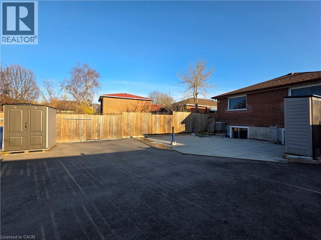 The property features a spacious paved area, a wooden fence, and a concrete patio - 62 Richwill Road Unit# Lower, Hamilton, ON - Outdoor
