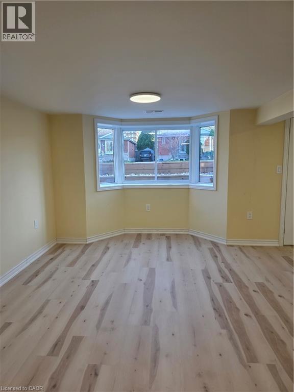 This room features light-toned flooring, a bay window with white trim, and a ceiling-mounted light fixture - 62 Richwill Road Unit# Lower, Hamilton, ON - Indoor Photo Showing Other Room