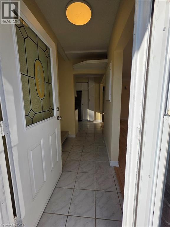 The entryway features a white door with decorative glass inserts, leading into a hallway with light-colored tile flooring and an overhead light fixture - 62 Richwill Road Unit# Upper, Hamilton, ON - Indoor Photo Showing Other Room