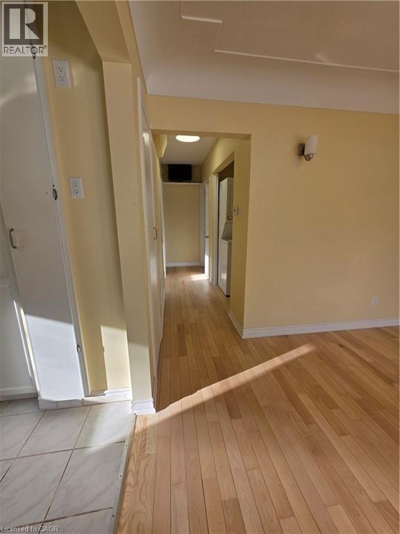 The property features light-colored hardwood flooring throughout the main living areas, complemented by warm-toned wall paint and white baseboards - 62 Richwill Road Unit# Upper, Hamilton, ON - Indoor Photo Showing Other Room