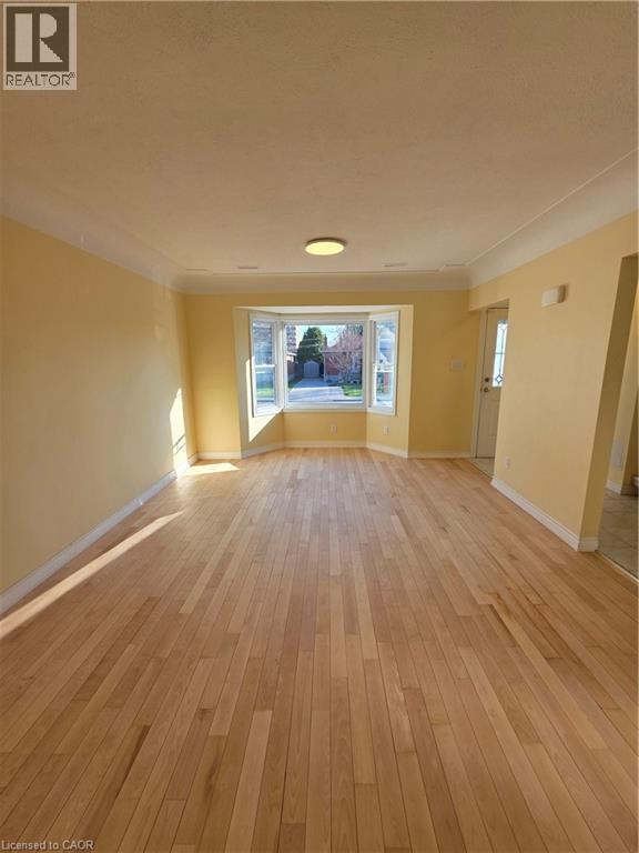 The property features an expansive room with light-toned hardwood flooring, a bay window providing ample natural light, and a ceiling light fixture - 62 Richwill Road Unit# Upper, Hamilton, ON - Indoor