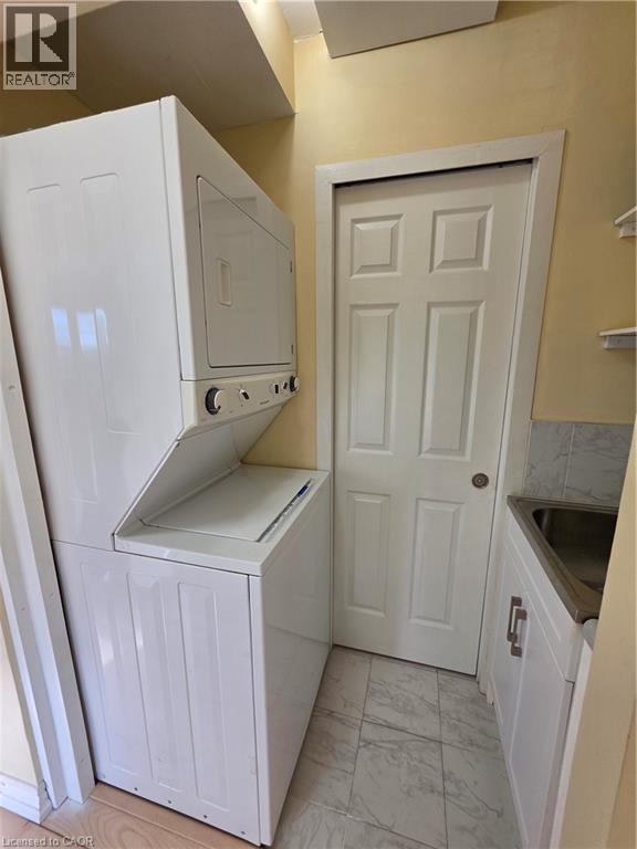 Laundry area featuring a stacked washer and dryer, tiled flooring, and a utility sink with white cabinetry - 62 Richwill Road Unit# Upper, Hamilton, ON - Indoor Photo Showing Laundry Room