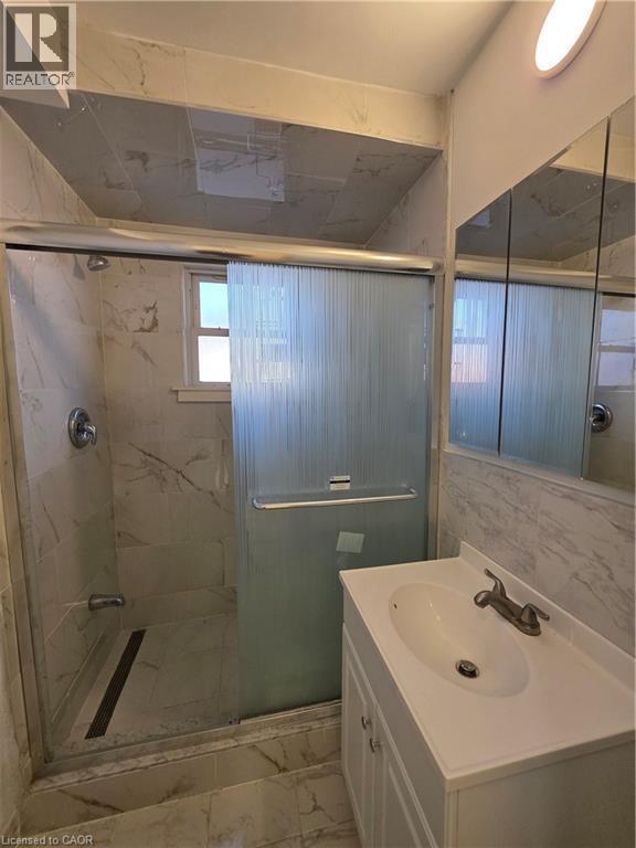 Bathroom featuring a shower with a sliding glass door, white marble-style wall and floor tiling, and a white vanity with a single sink - 62 Richwill Road Unit# Upper, Hamilton, ON - Indoor Photo Showing Bathroom