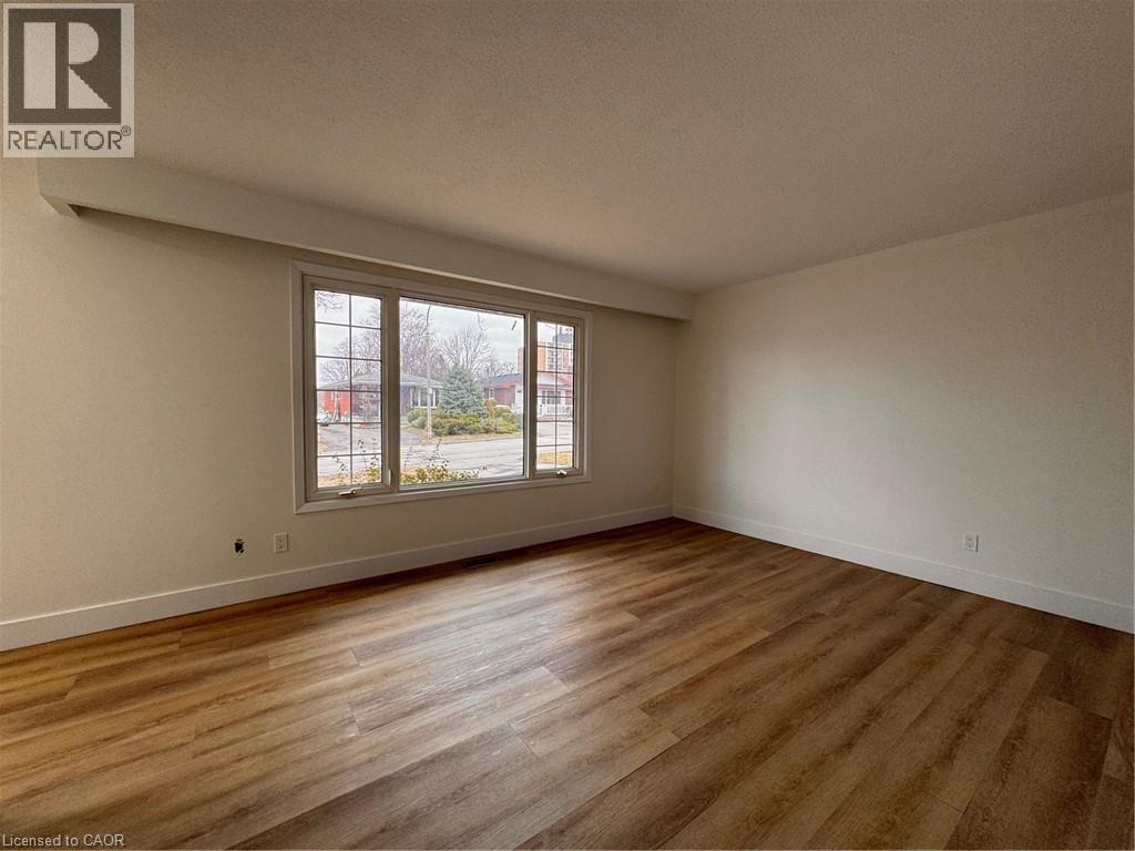 This inviting room features warm-toned flooring, a large window providing views of the outdoors, and a neutral color palette throughout - 23 Arrowhead Crescent Unit# Upper, Kitchener, ON - Indoor Photo Showing Other Room
