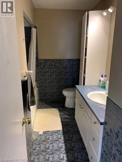 Full bathroom with vanity, tile walls, shower / bath combo, wainscoting, and dark tile patterned floors - 65 Cardill Crescent Unit# A, Waterloo, ON - Indoor Photo Showing Bathroom