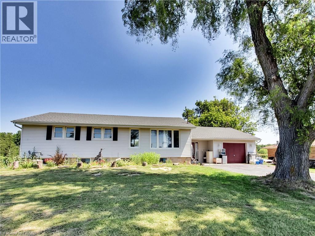 Ranch-style residence featuring light-colored siding, black window shutters, and an attached two-car garage with a red door - 9183 Silver Street, Caistor Centre, ON - Outdoor