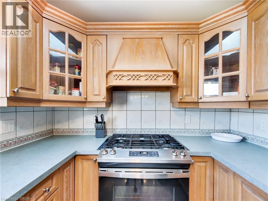 Kitchen featuring light wood cabinetry, glass-front upper cabinets, a custom wood range hood, a tiled backsplash, and light-toned countertops - 9183 Silver Street, Caistor Centre, ON - Indoor Photo Showing Kitchen