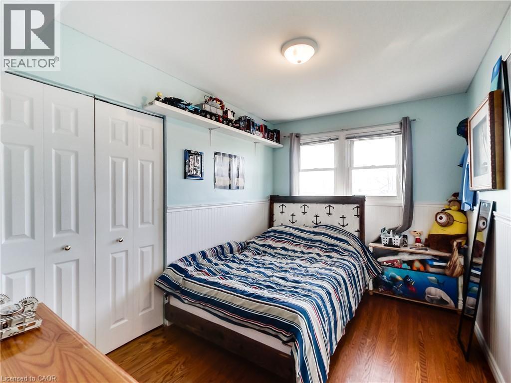 Bedroom featuring wood-finish flooring, two sets of bi-fold closet doors, a double window with curtains, and a ceiling-mounted light fixture - 9183 Silver Street, Caistor Centre, ON - Indoor Photo Showing Bedroom