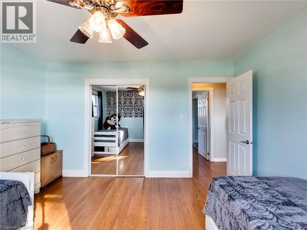 Hardwood-finish flooring extending throughout, ceiling fan with integrated lighting, mirrored sliding closet doors, and a paneled interior door - 9183 Silver Street, Caistor Centre, ON - Indoor Photo Showing Bedroom