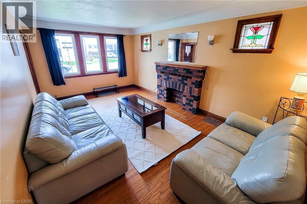 Living area featuring wood-finish flooring, a brick-detailed fireplace, and bay windows with wood trim - 66 Cline Avenue Unit# Main Floor, Hamilton, ON - Indoor Photo Showing Living Room