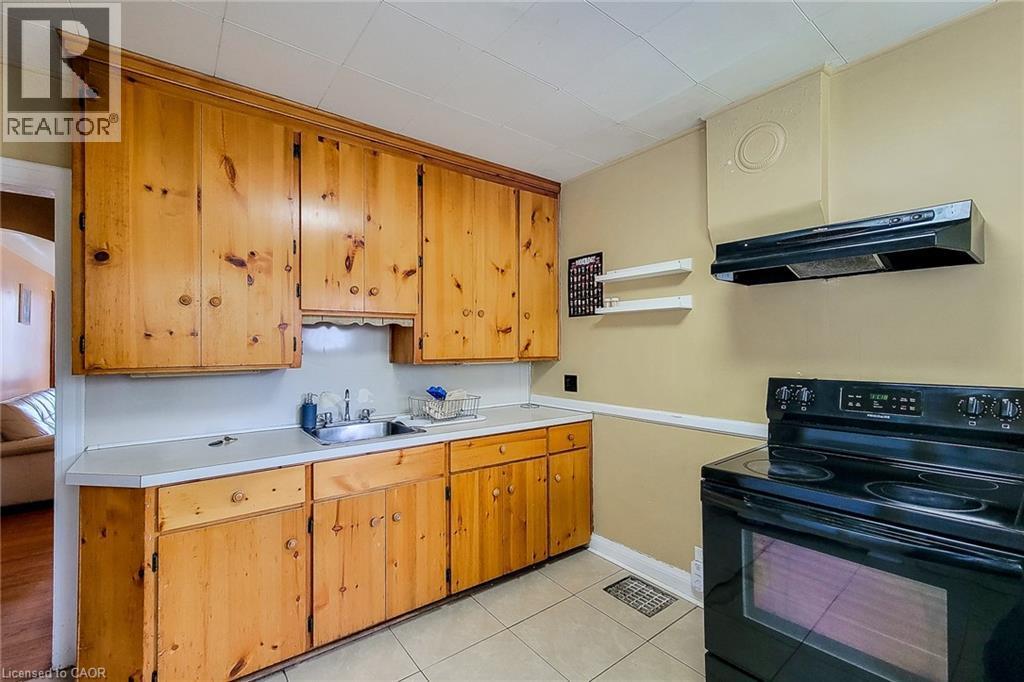 Kitchen featuring natural wood cabinetry, light-toned countertops, a stainless steel sink, black range, and tiled flooring - 66 Cline Avenue Unit# Main Floor, Hamilton, ON - Indoor Photo Showing Kitchen