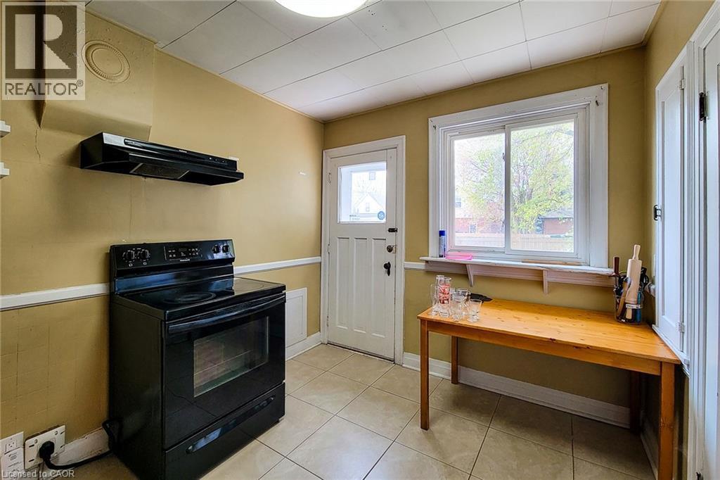 Kitchen featuring a black electric range with an overhead exhaust fan, a white paneled door, and a sliding window - 66 Cline Avenue Unit# Main Floor, Hamilton, ON - Indoor