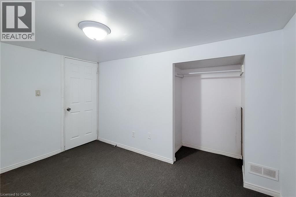 Room featuring dark gray carpet flooring, white walls, a single paneled door, and an open closet space with a hanging rod - 66 Cline Avenue Unit# Main Floor, Hamilton, ON - Indoor Photo Showing Other Room