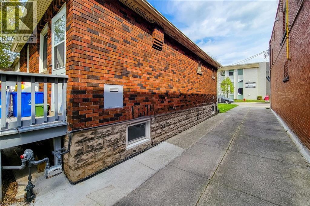 Brick exterior with a stone foundation, featuring a ground-level window and a raised deck with a wooden railing - 66 Cline Avenue Unit# Main Floor, Hamilton, ON - Outdoor With Exterior