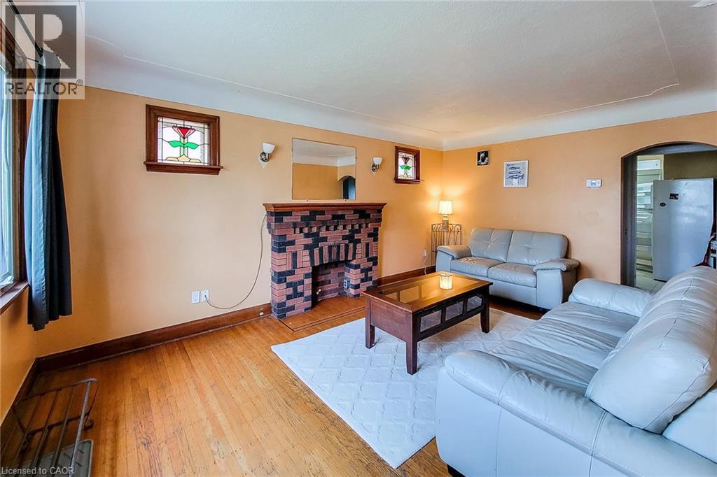 Living area featuring wood-finish flooring, a brick-detailed fireplace with a wooden mantel, and a stained-glass window accent - 66 Cline Avenue Unit# Main Floor, Hamilton, ON - Indoor Photo Showing Living Room With Fireplace