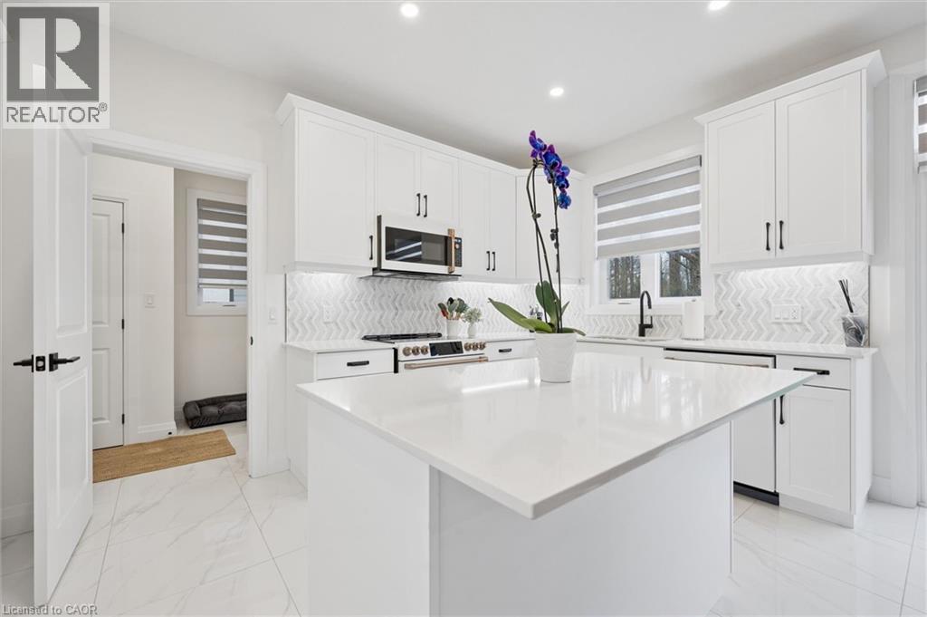 Modern kitchen featuring a large central island with a solid surface countertop, white shaker-style cabinetry, stainless steel appliances, a chevron-patterned tile backsplash, and recessed lighting - 213 Fallowfield Drive, Kitchener, ON - Indoor Photo Showing Kitchen With Upgraded Kitchen