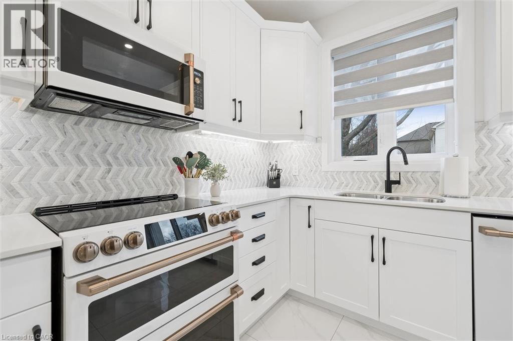 Contemporary kitchen featuring white cabinetry with matte black hardware, a chevron pattern tile backsplash, and light-tone countertops - 213 Fallowfield Drive, Kitchener, ON - Indoor Photo Showing Kitchen With Double Sink With Upgraded Kitchen