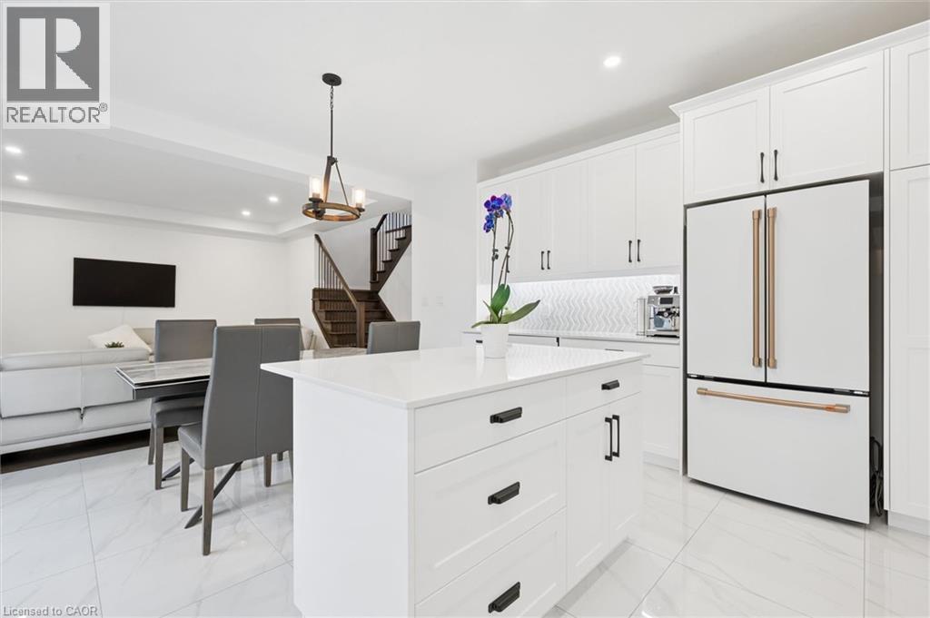 Open-concept kitchen and dining area featuring a central island, white cabinetry with dark hardware, a white tile backsplash, and large format floor tiling - 213 Fallowfield Drive, Kitchener, ON - Indoor Photo Showing Kitchen