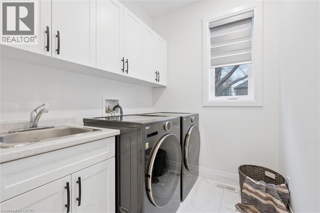 Dedicated laundry room featuring white cabinetry with matte black hardware, an integrated utility sink with a chrome faucet, a stone-finish countertop, and a window for natural light - 213 Fallowfield Drive, Kitchener, ON - Indoor Photo Showing Laundry Room