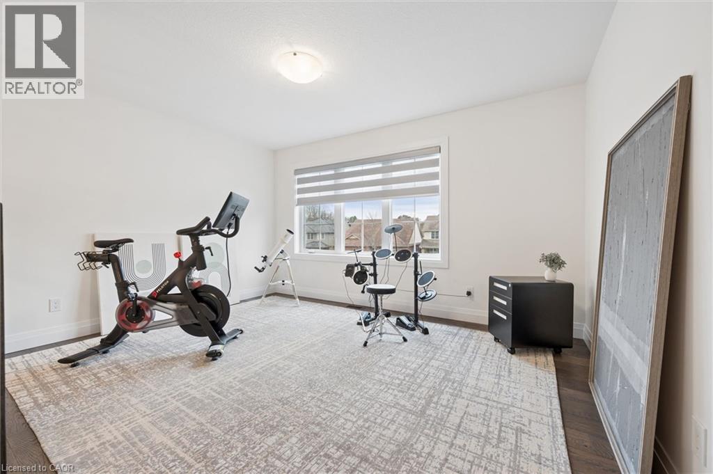 Bright room featuring a large window with blinds, dark wood-finish flooring, white baseboards, and a ceiling-mounted light fixture - 213 Fallowfield Drive, Kitchener, ON - Indoor Photo Showing Gym Room