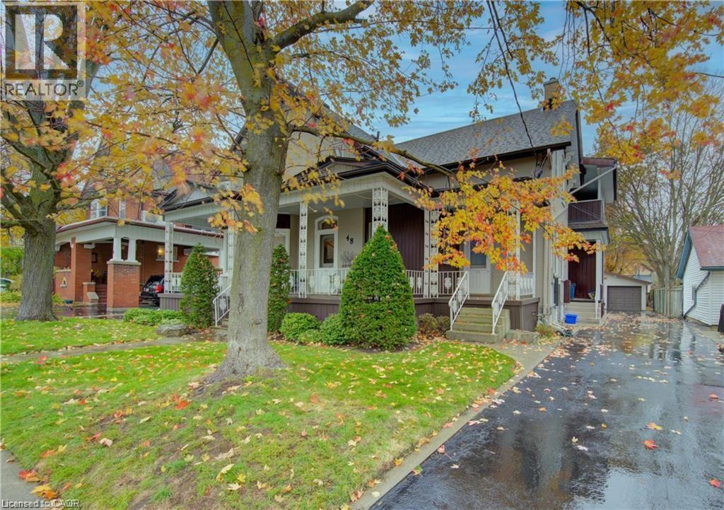 Charming property exterior featuring a covered front porch with decorative railing, a well-maintained lawn, and a paved driveway leading to a detached garage - 48 Dupont Street, Waterloo, ON - Outdoor With Facade