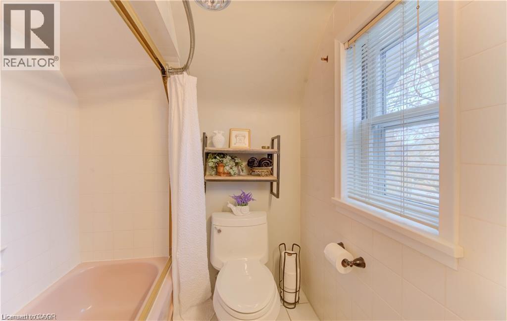 The bathroom features a bathtub, a toilet, and a window with blinds providing natural light - 48 Dupont Street, Waterloo, ON - Indoor Photo Showing Bathroom