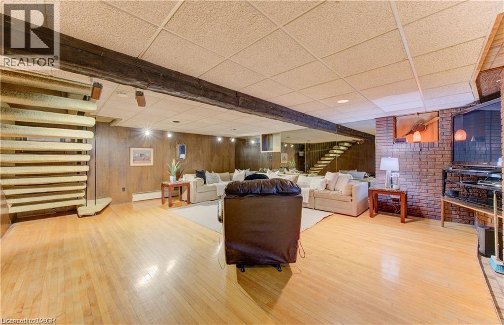 Spacious recreation room featuring light wood flooring, wood paneled walls, exposed wooden beams, and a brick accent wall with a built-in shelf - 48 Dupont Street, Waterloo, ON - Indoor