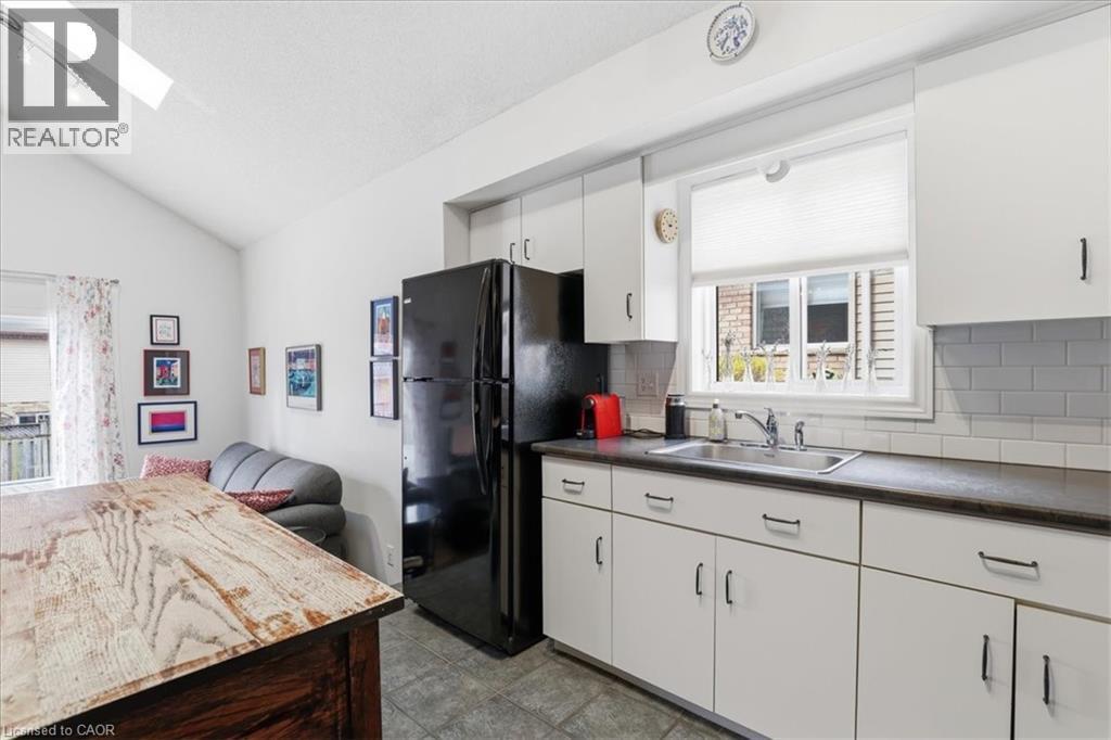 The kitchen features white cabinetry with dark pulls, a black refrigerator, and a window above the sink - 110 Milton Avenue, Cambridge, ON - Indoor Photo Showing Kitchen