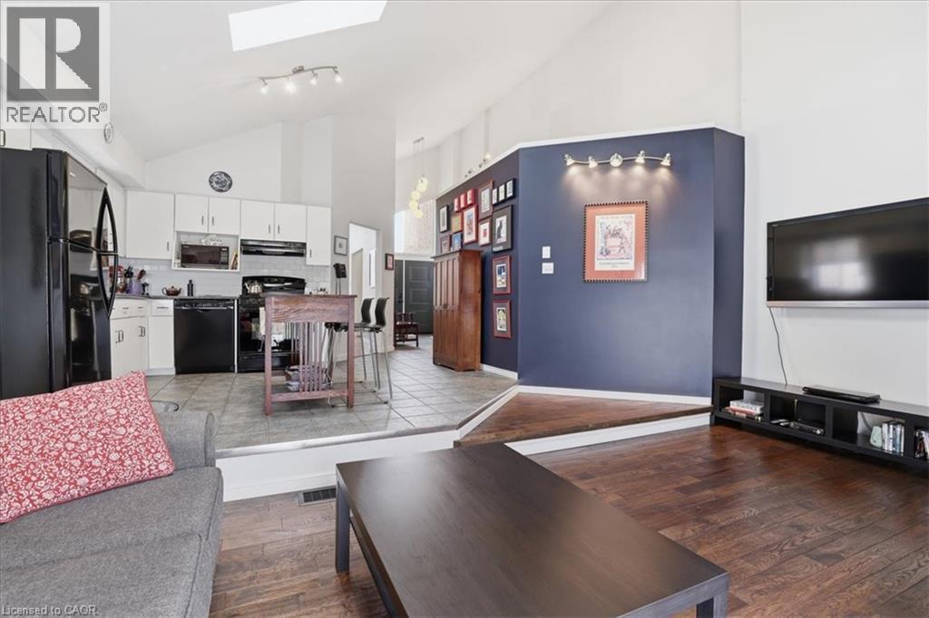 The property features an open-concept layout with vaulted ceilings, a kitchen with white cabinetry and black appliances, and a living area with hardwood flooring - 110 Milton Avenue, Cambridge, ON - Indoor Photo Showing Living Room