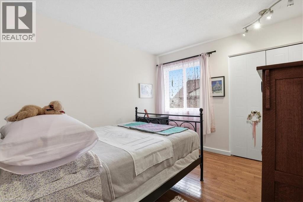 This room features hardwood floors, a window with sheer curtains, track lighting, and a white closet with sliding doors - 110 Milton Avenue, Cambridge, ON - Indoor Photo Showing Bedroom