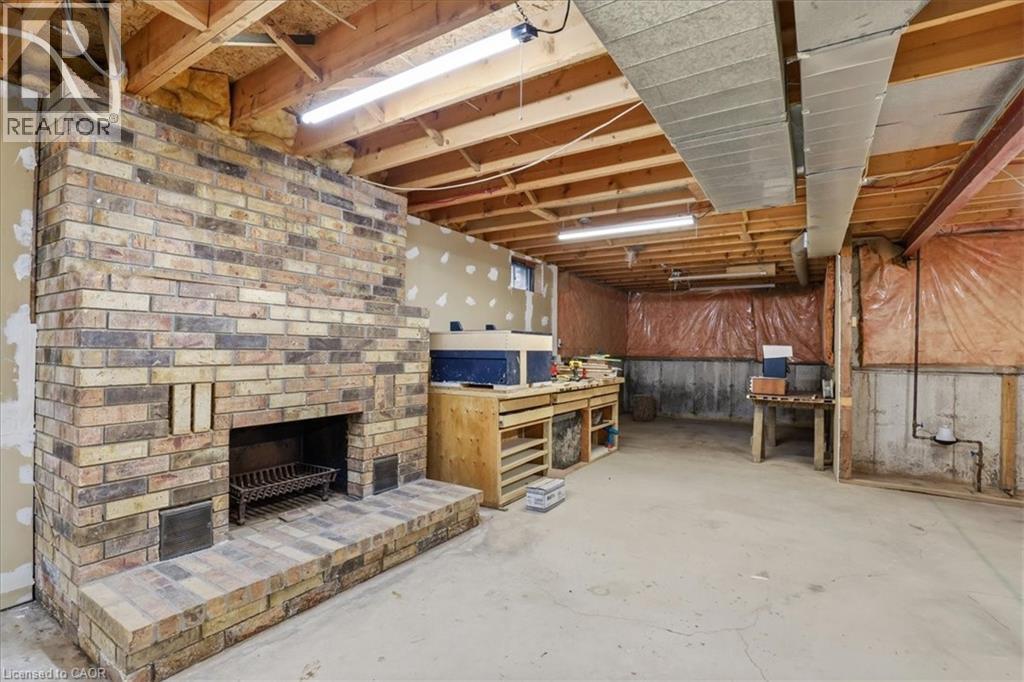 Spacious basement area featuring exposed ceiling joists, concrete flooring, and a large brick fireplace with a hearth - 110 Milton Avenue, Cambridge, ON - Indoor With Fireplace