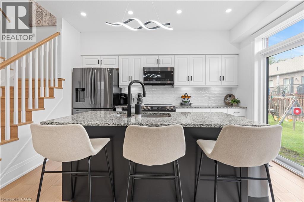 Modern kitchen featuring a black island with a speckled countertop, white cabinetry with black hardware, and stainless steel appliances - 1026 Wright Drive, Midland, ON - Indoor