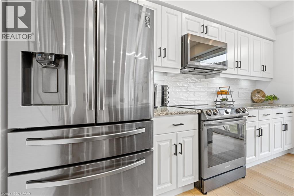 Modern kitchen featuring stainless steel appliances, white shaker-style cabinetry with dark hardware, a white subway tile backsplash, and light wood-finish flooring - 1026 Wright Drive, Midland, ON - Indoor Photo Showing Kitchen With Upgraded Kitchen