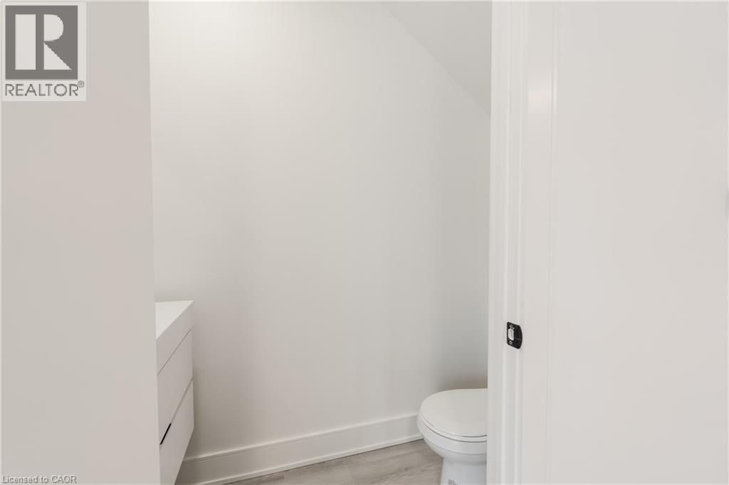 This powder room features a modern white vanity and a toilet, set against light-colored walls - 144 Everett Common, St. Catharines, ON - Indoor Photo Showing Bathroom
